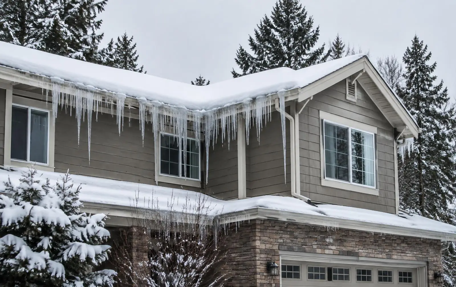 Home roof edge with a thick ice dam and icicles in winter